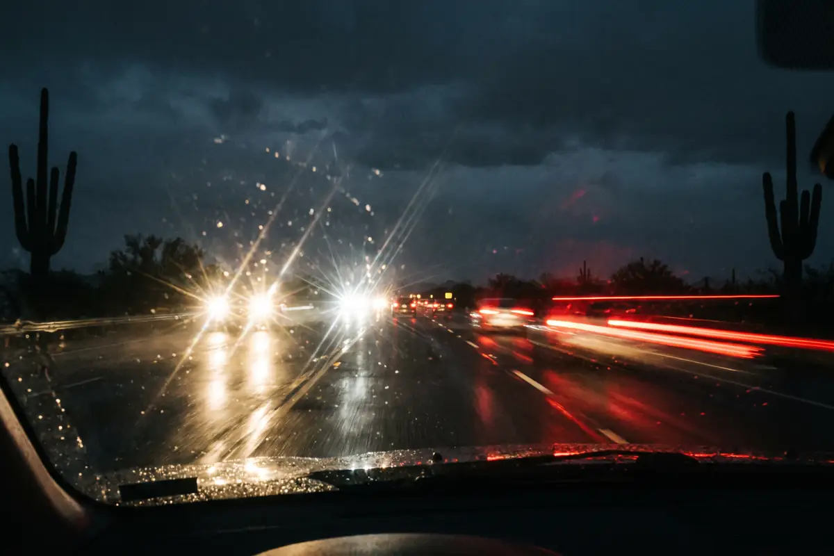 A dark Arizona highway at night seen through a rain-flecked windshield with oncoming headlights flaring